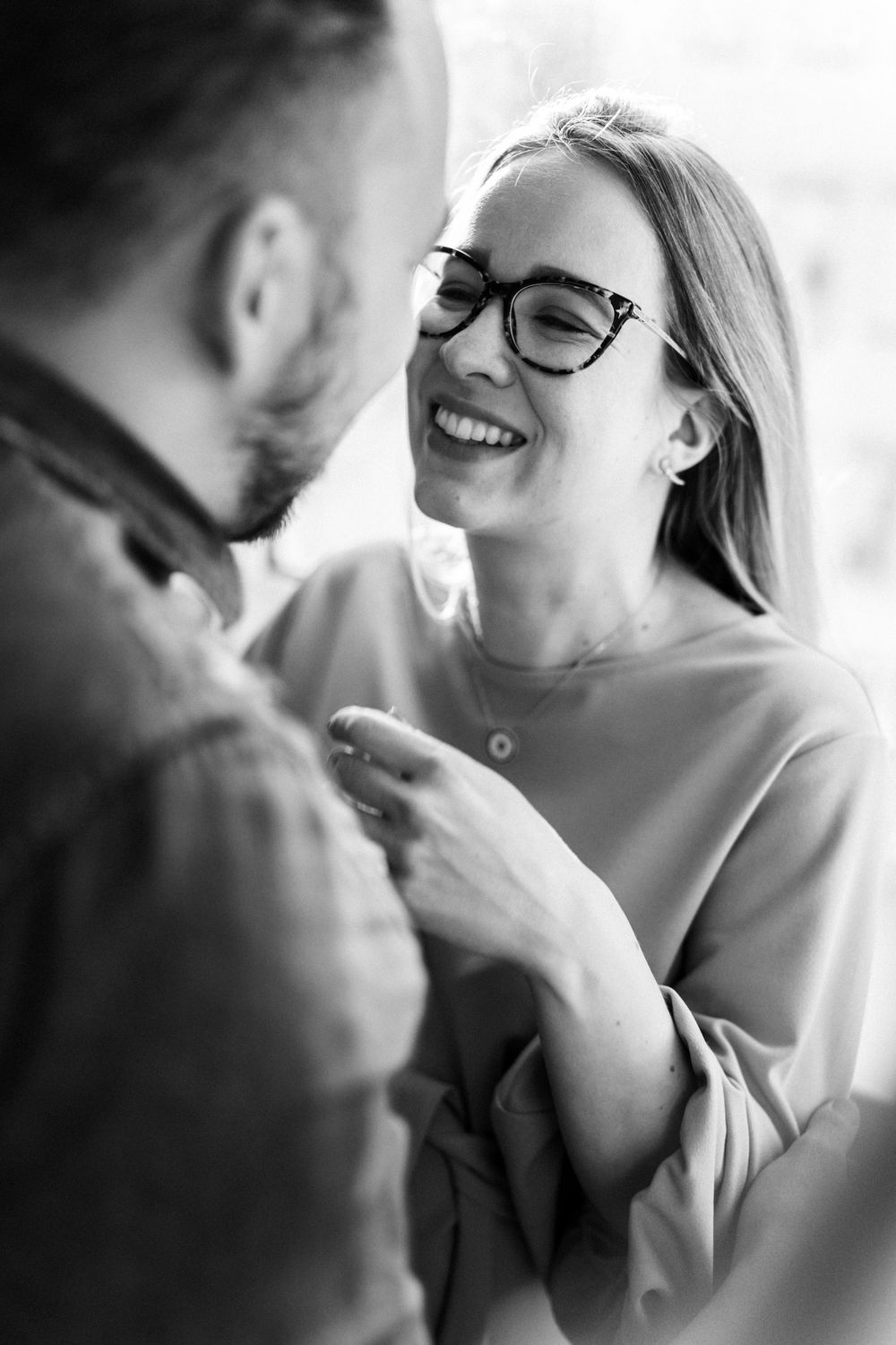 A couple shares a lighthearted moment together by a window.