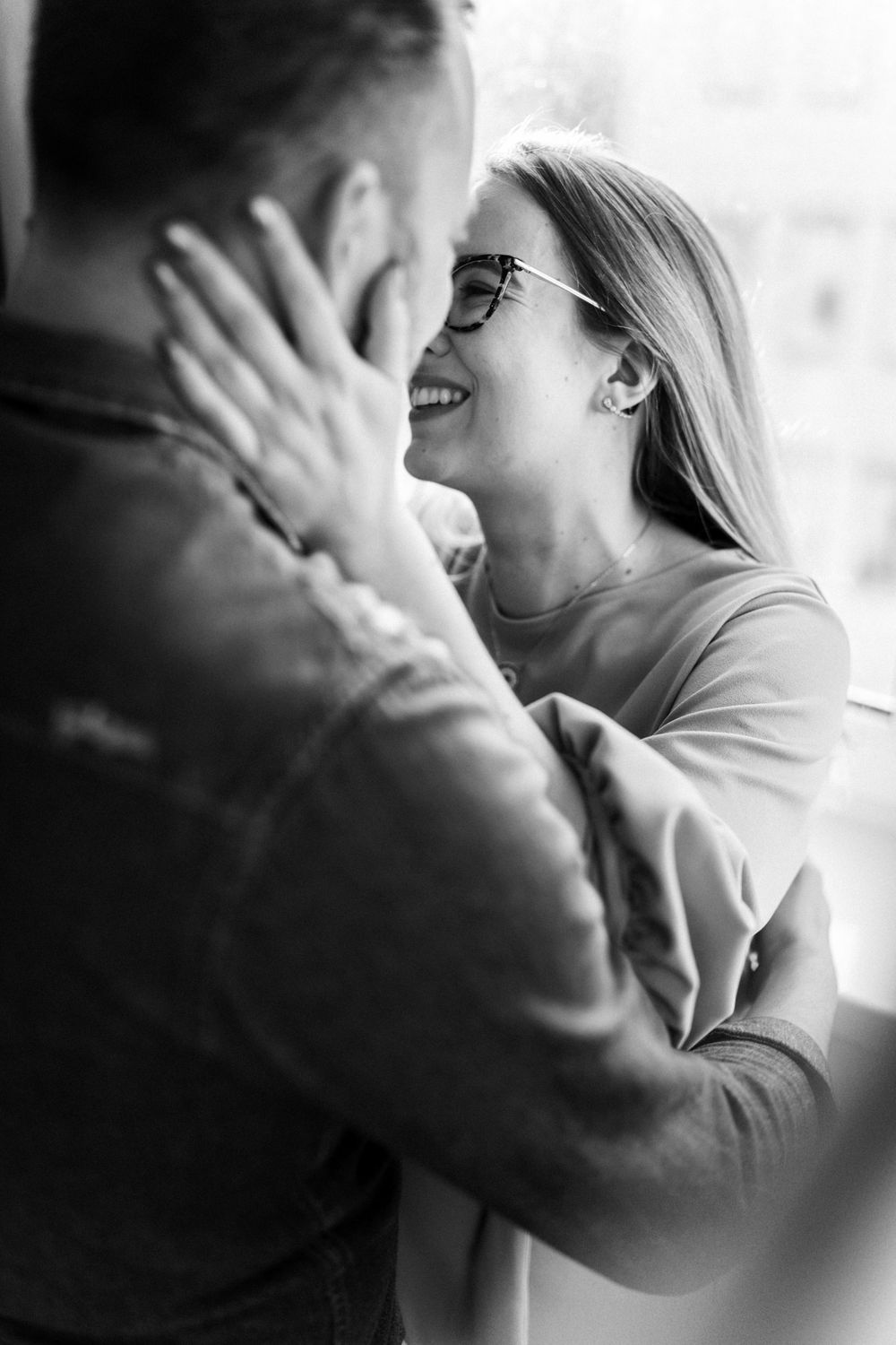 A tender romantic moment captured in black and white as a couple shares a loving embrace by a window.
