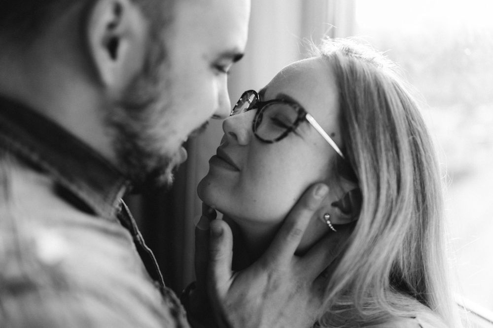 An intimate black and white portrait of a couple sharing a romantic kiss while wearing glasses.