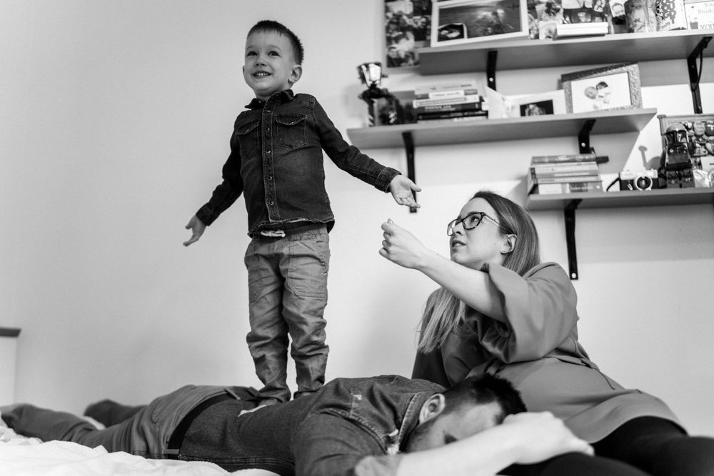 A playful family scene on a bed with energetic interactions and shelf decorations in the background.