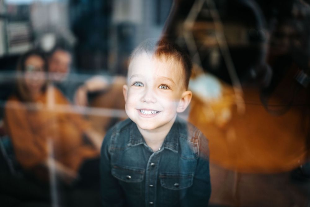 Soft focus portrait through glass window showing joyful expression and denim shirt.