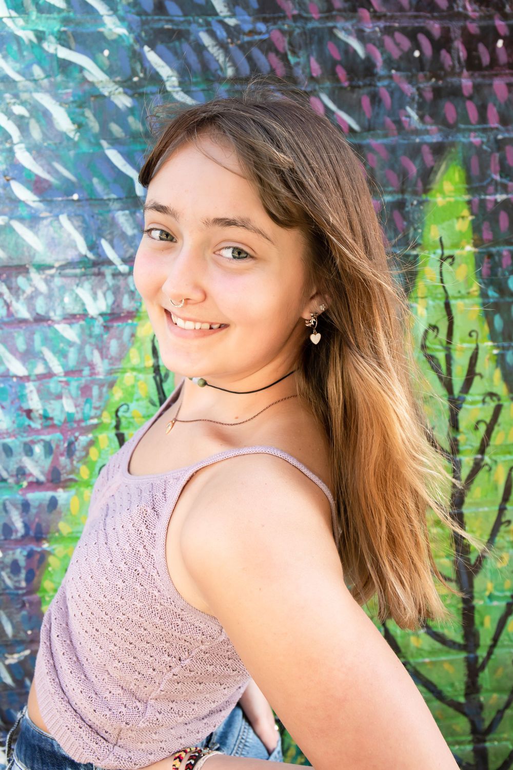Portrait against vibrant street art wall wearing pink tank top and choker necklace.