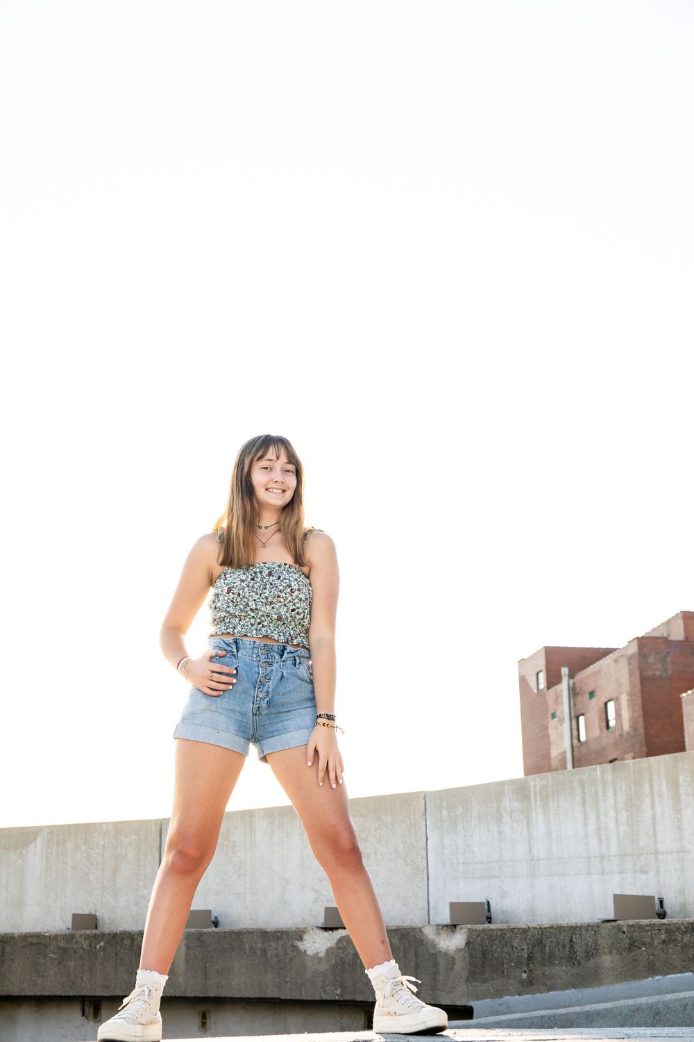 Person in floral top and denim poses on concrete barrier against white background.