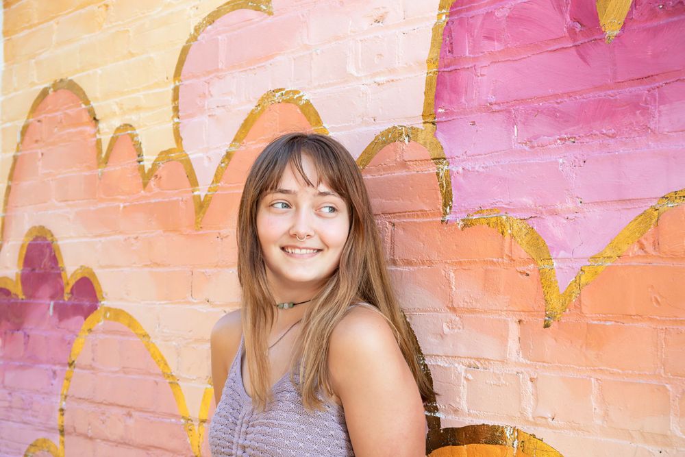 Portrait against colorful pink and orange painted brick wall mural.