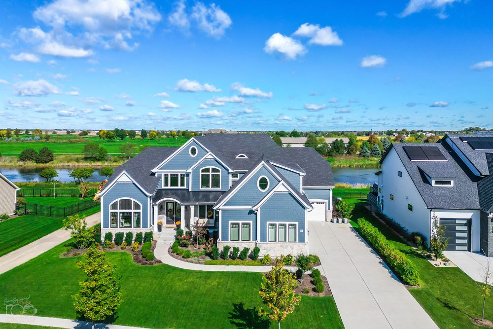 Aerial view of large blue craftsman style home with extensive driveway in suburban setting.