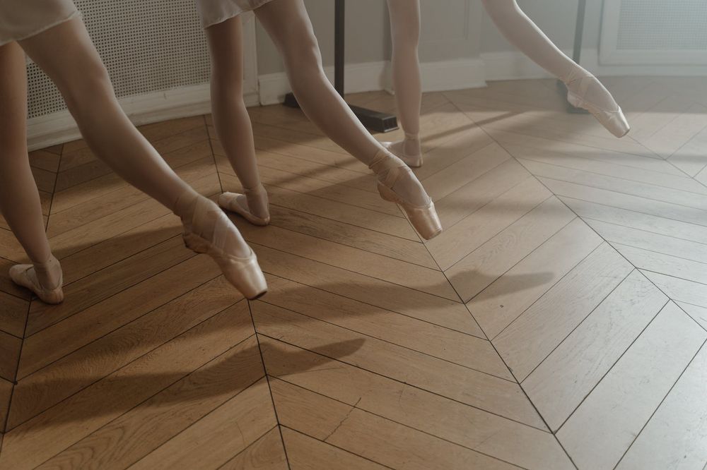 Ballet shoes and feet in pointe position against a herringbone wooden floor.