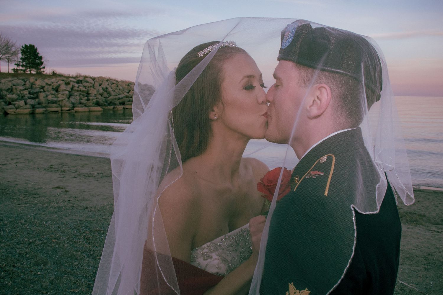 Bride and groom sharing a kiss under her veil on the beach during sun set in Stoney Creek, Ontario.