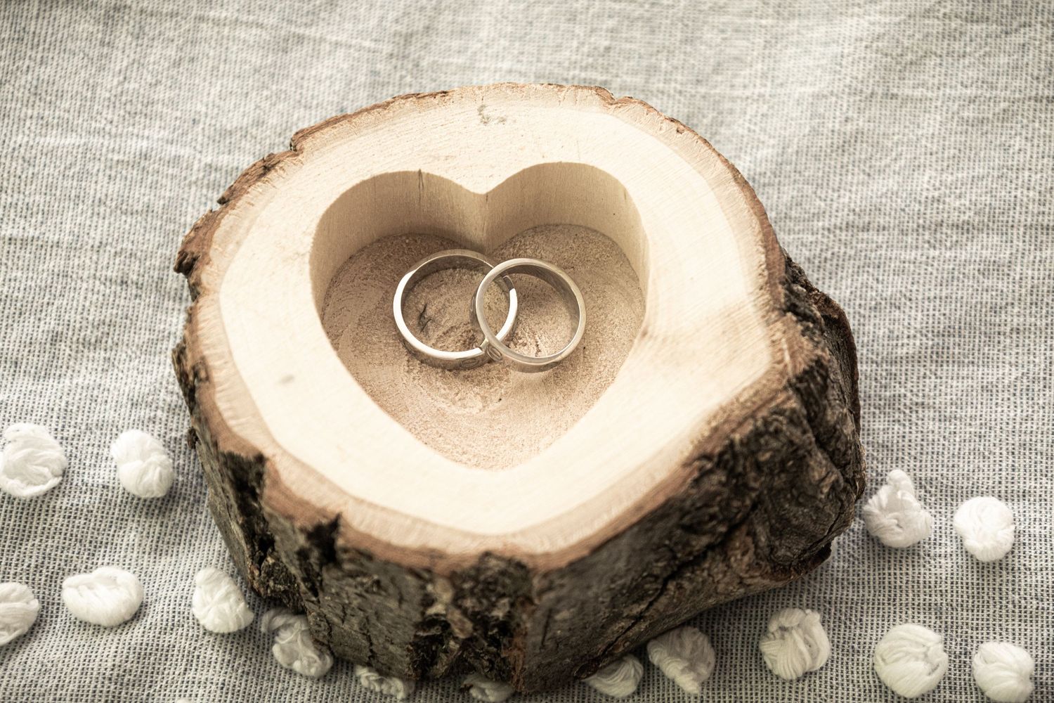 Rustic wood slice wedding ring display with pearls and carved heart detail.