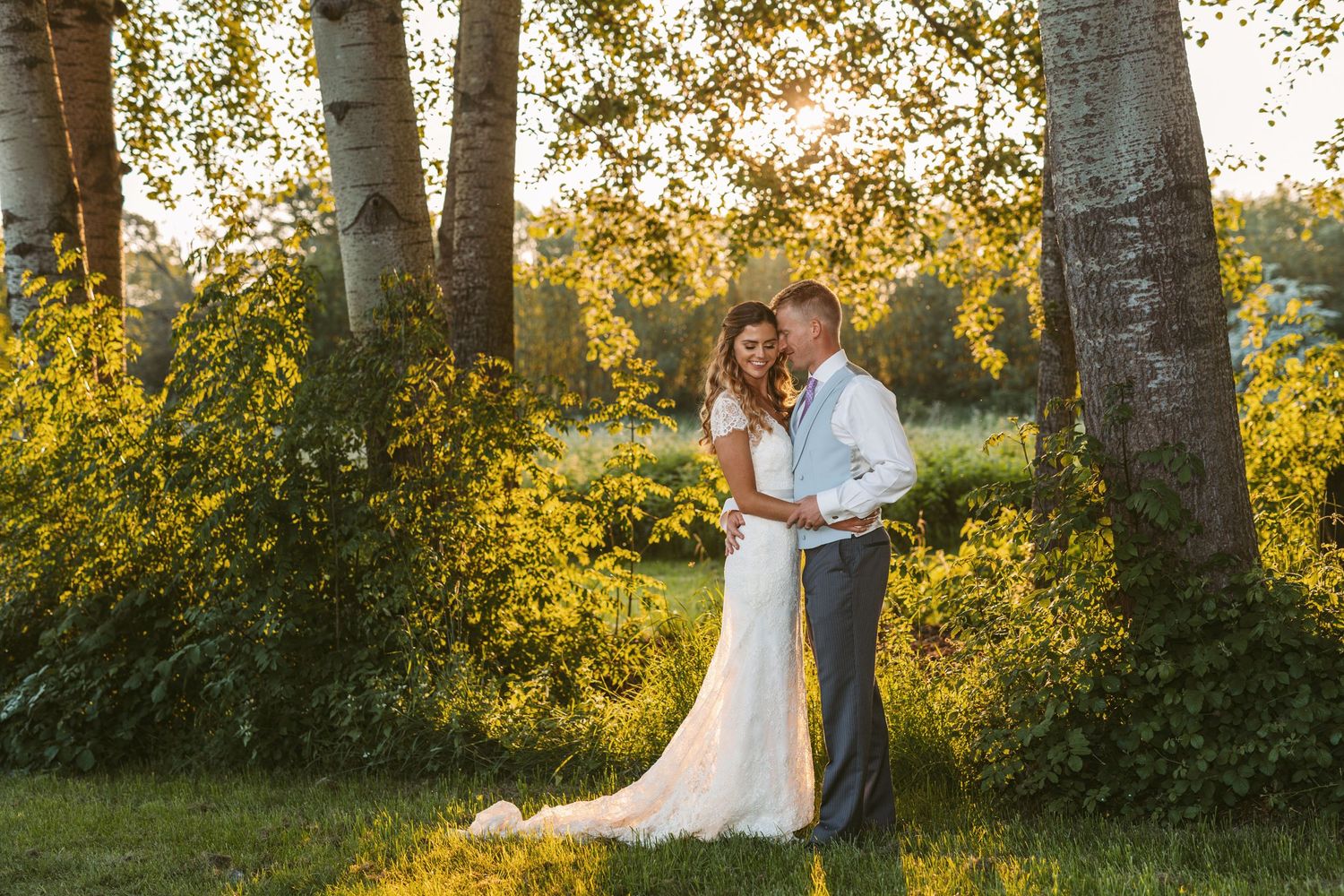 Bride and groom newly wed and embracing in beautiful dappled sunlight with willow trees behind them