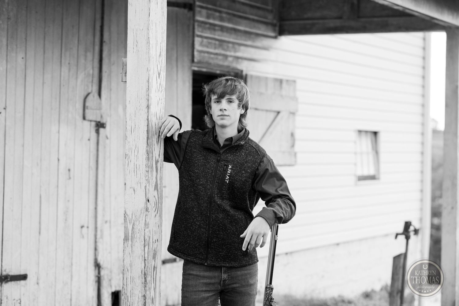Black and white photo of figure leaning against white barn doorframe in casual pose.