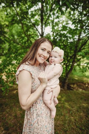 A joyful moment shared between parent and baby under green summer trees.