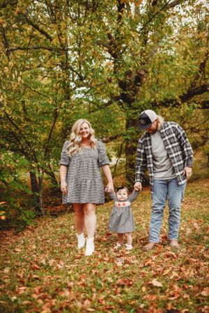 A family walks through fallen autumn leaves in a wooded area during fall season.