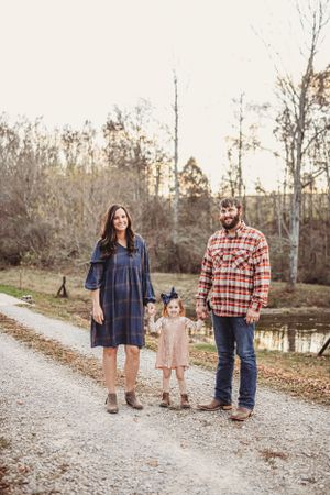 A family in plaid and denim outfits stands together on a gravel path near a pond.