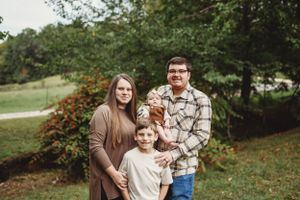 A family poses together outdoors during autumn with fall foliage in the background.