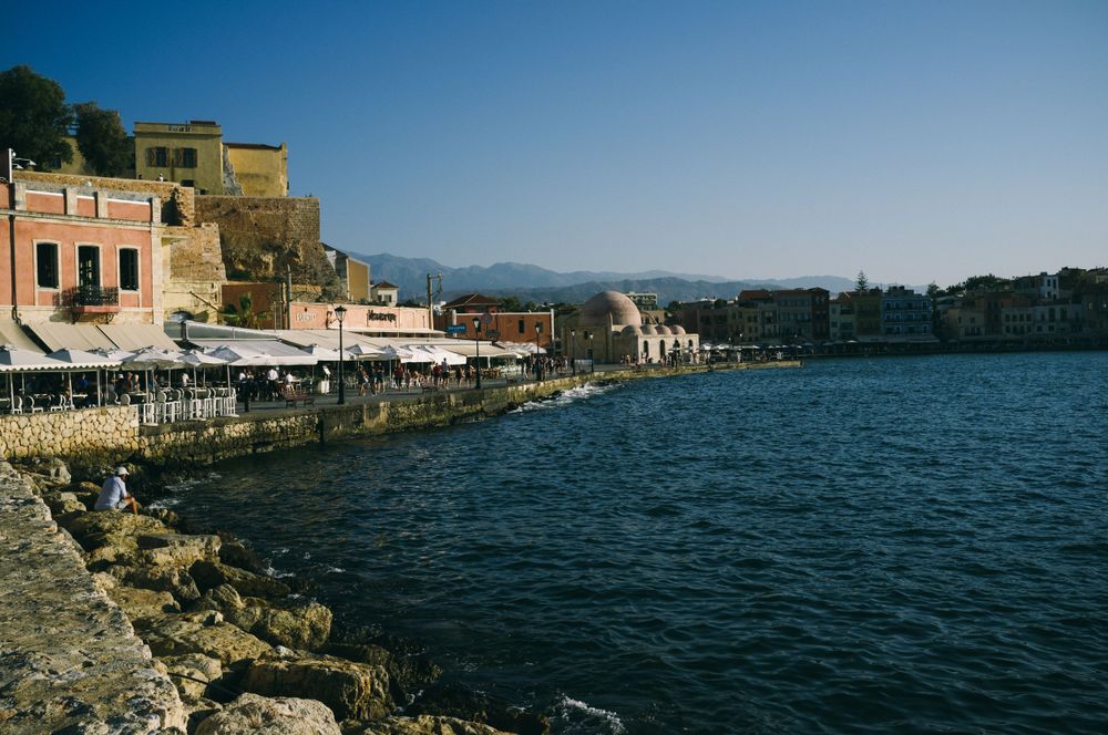 Panoramic view of a Mediterranean coastal town with historic buildings and blue waters.