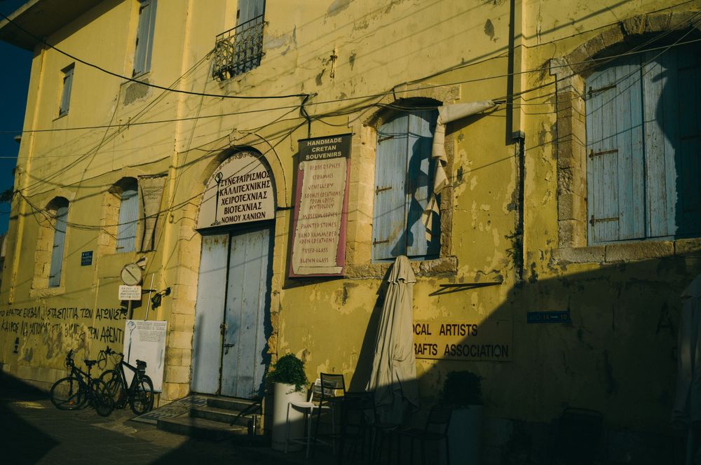 Row of yellow buildings with weathered facades and shutters along a narrow street.