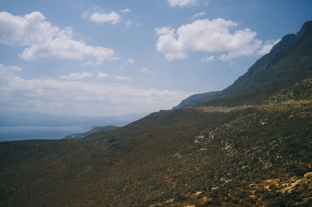 Panoramic mountain landscape with rugged terrain under blue skies and white clouds.