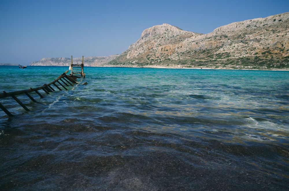 Coastal seascape with rocky cliffs and turquoise Mediterranean waters under clear blue sky.