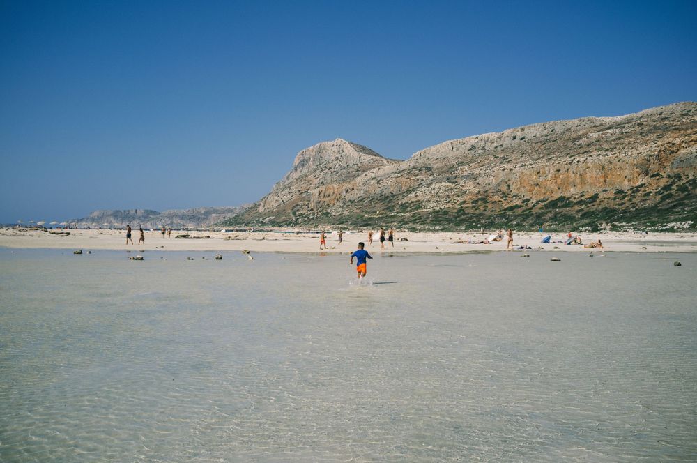 Wide sandy beach with distant mountains and scattered beachgoers on a sunny day.