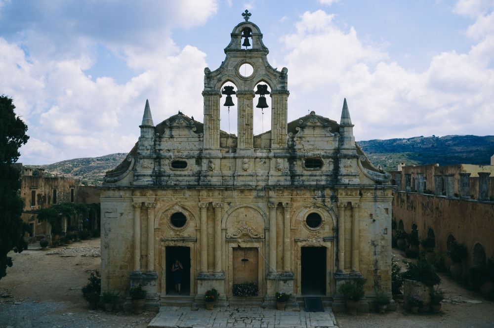 Historic stone monastery with bell towers and arched entrances under cloudy sky in Greece.