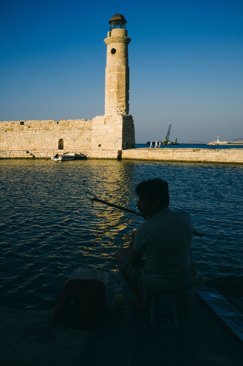 Lighthouse silhouetted against blue sea and sky at sunset.