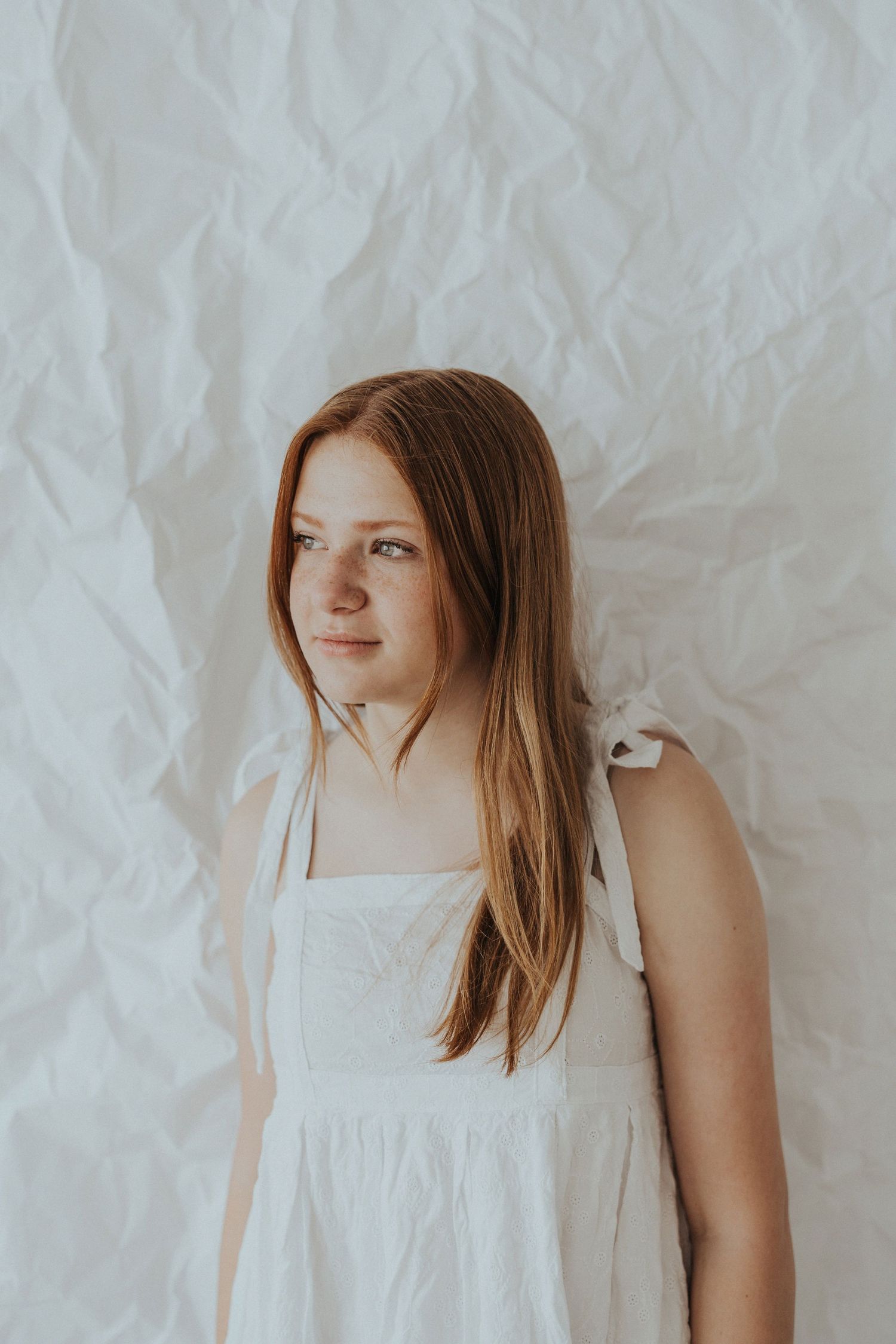 A redhead girl stands against a white paper backdrop