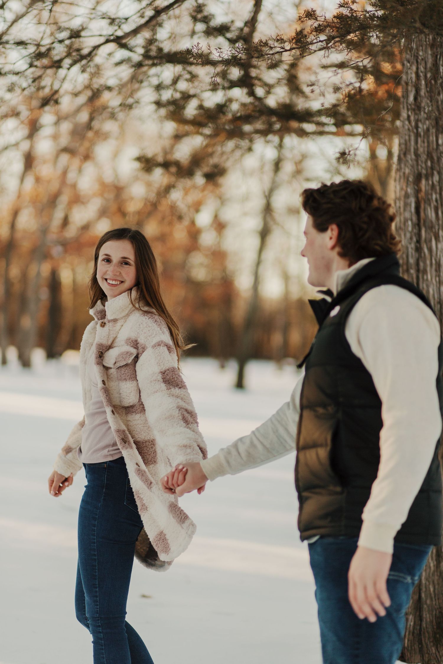 Couple walking together through snowy forest path in winter attire.