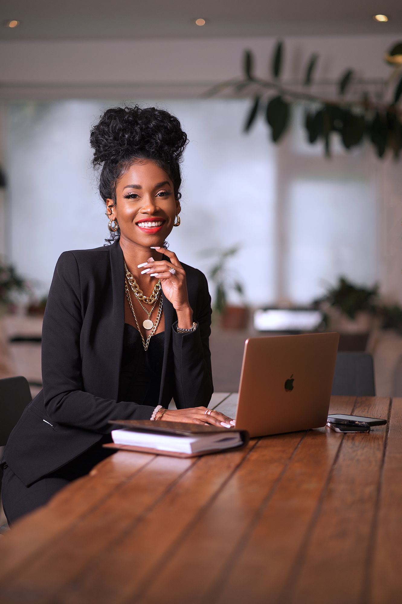 Professional in black blazer working on laptop with statement jewelry and natural updo hairstyle.