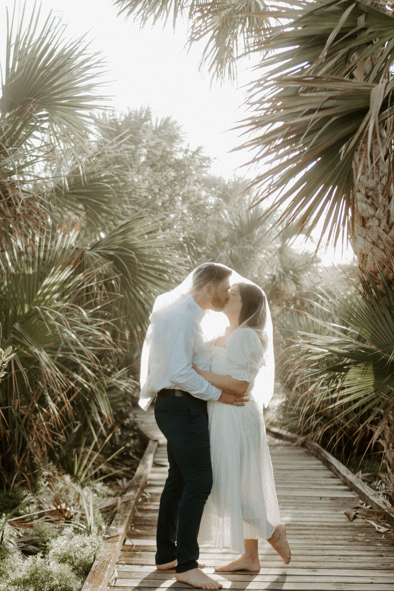 Elopement Couple kissing at the beach with a veil over their heads at sunset in New Smyrna Beach FL