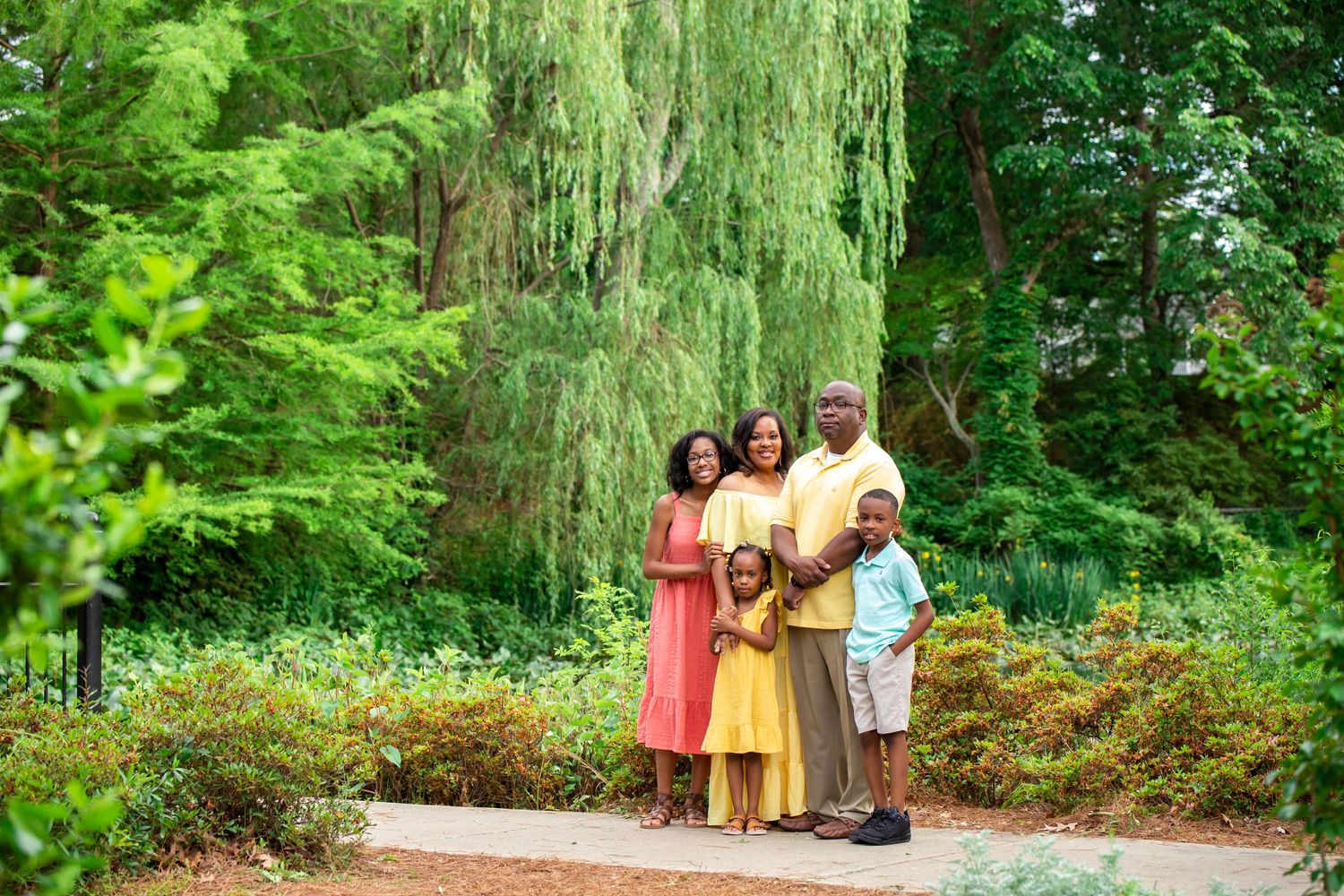 Family group in colorful summer dresses standing beneath weeping willow tree.