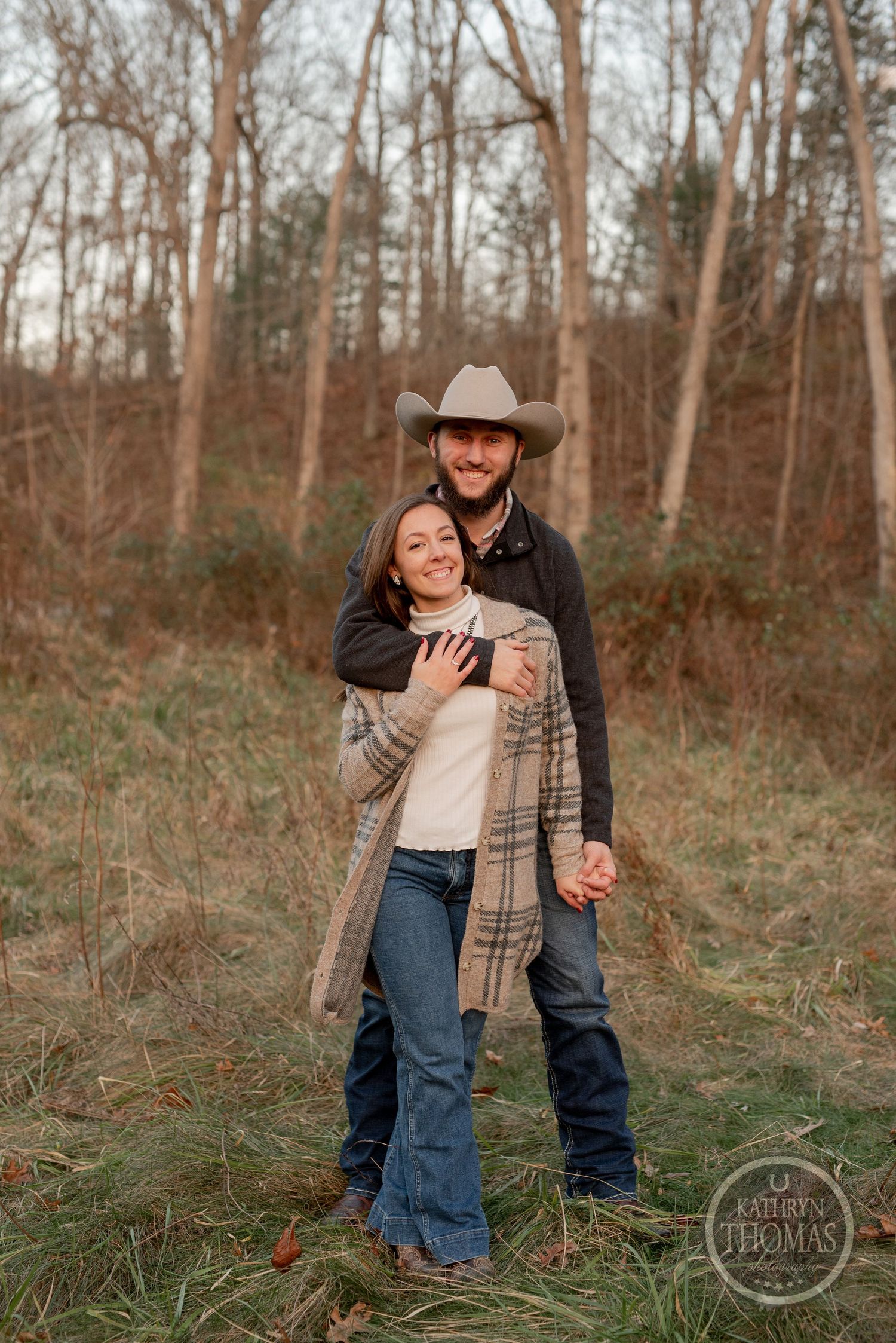 A sweet outdoor portrait of a couple in western attire against a wooded backdrop.