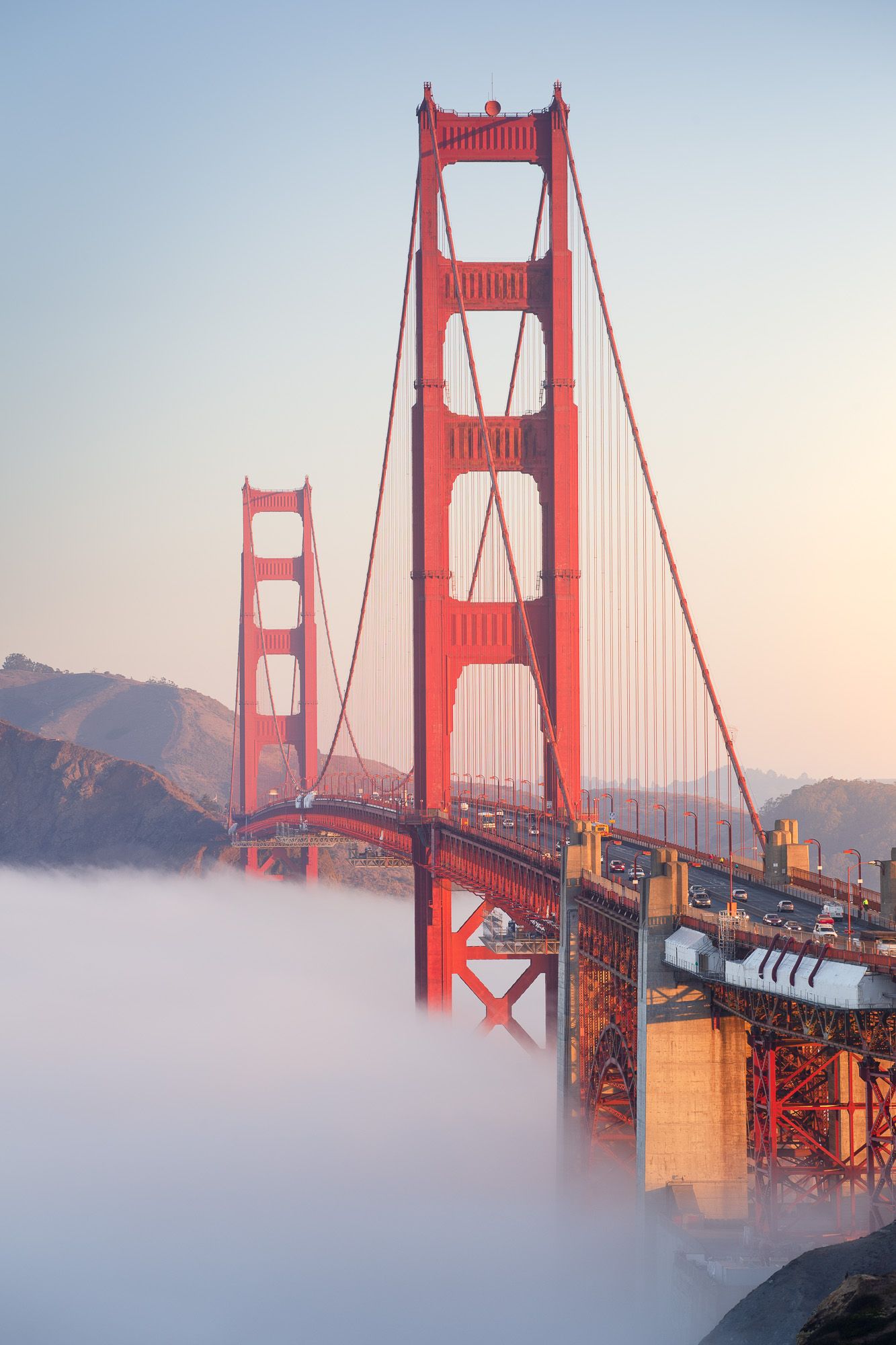 The iconic Golden Gate Bridge emerges from dense fog during sunrise in San Francisco, California.