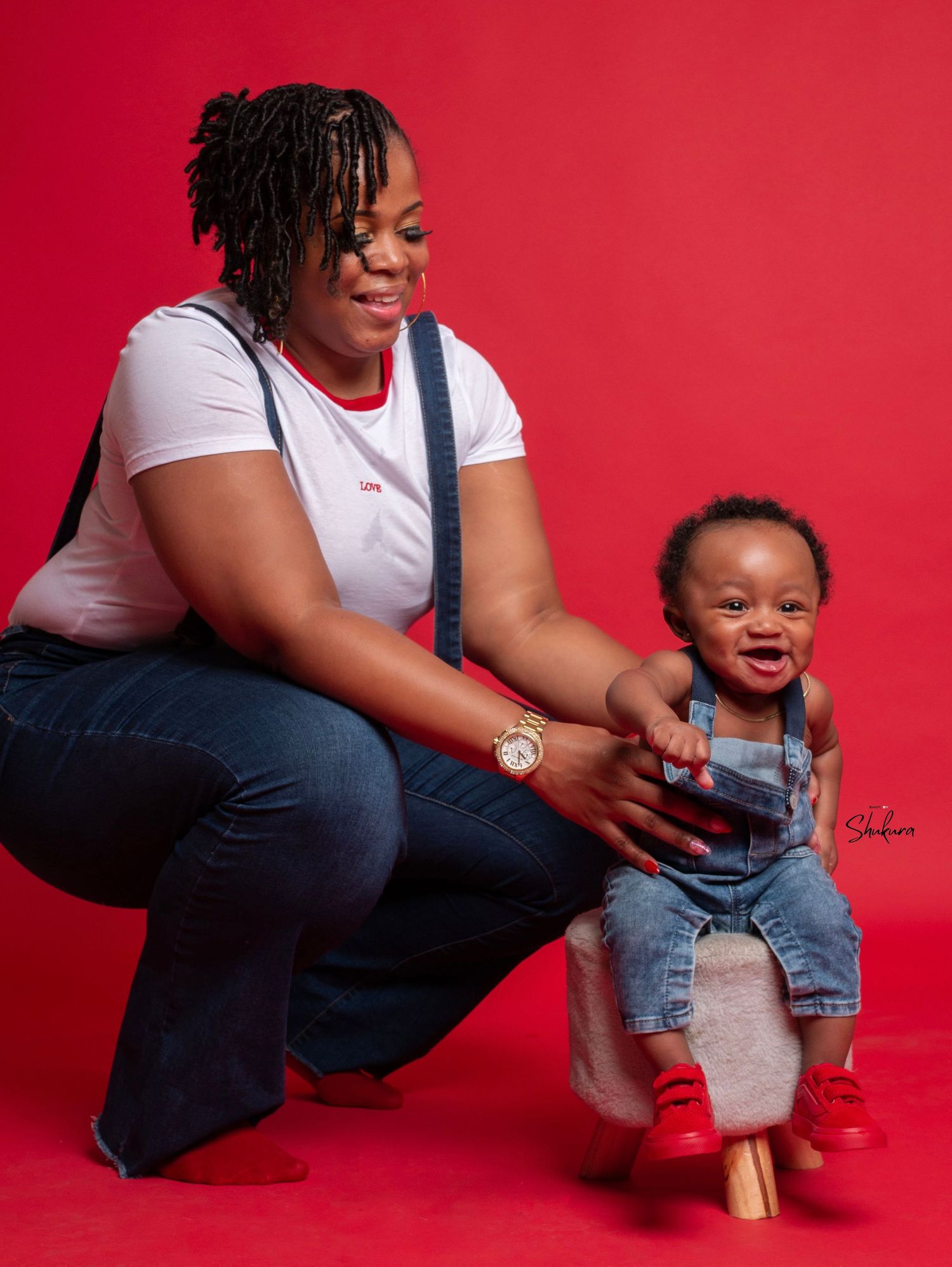Mother and toddler share playful moment during studio photoshoot against red backdrop.