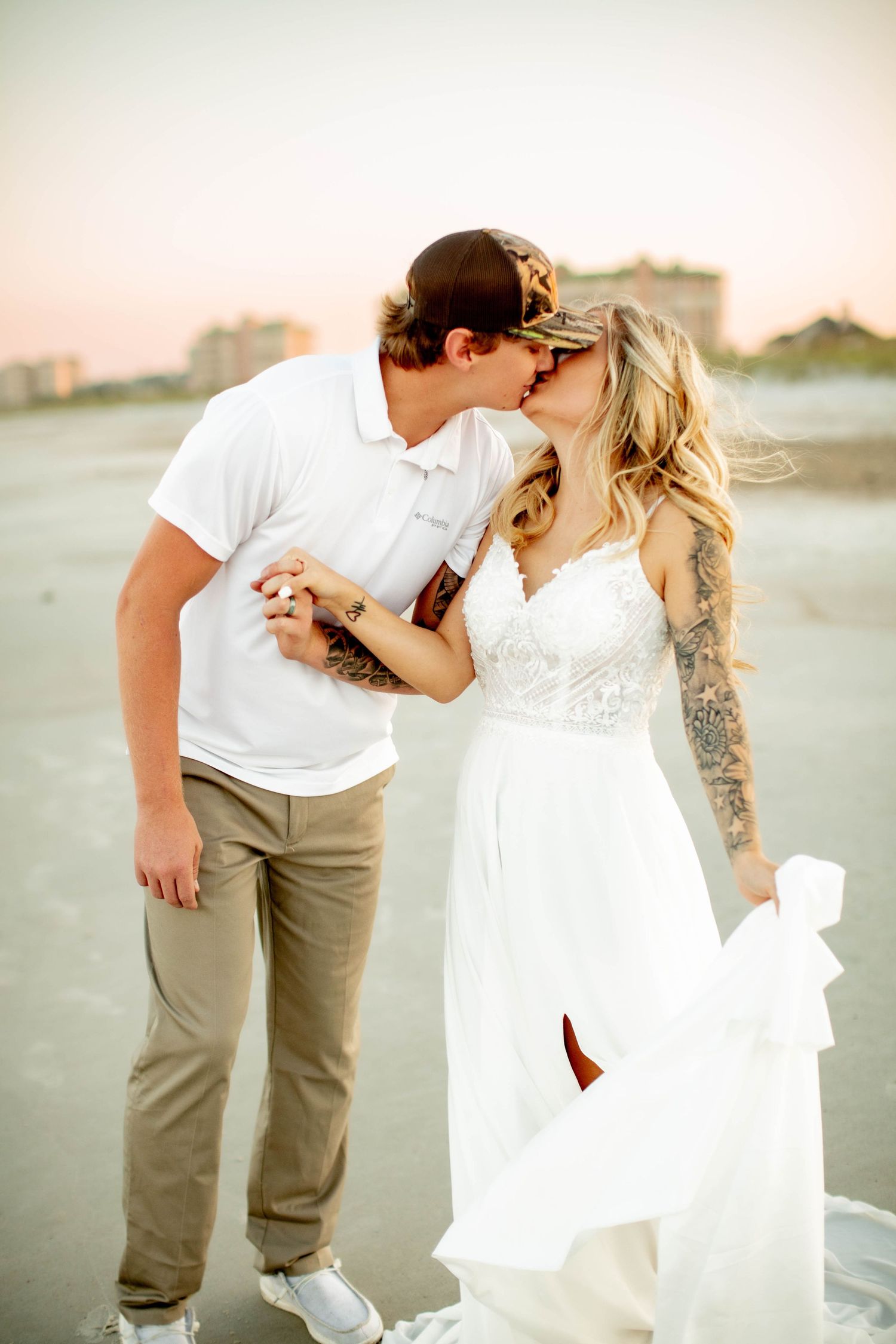 Couple in casual wedding attire share a romantic moment on a beach at sunset.