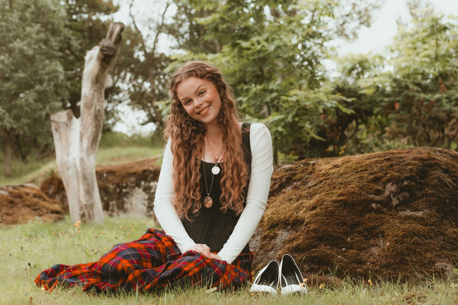 Person in white sweater sitting on fallen tree trunk in outdoor nature setting.