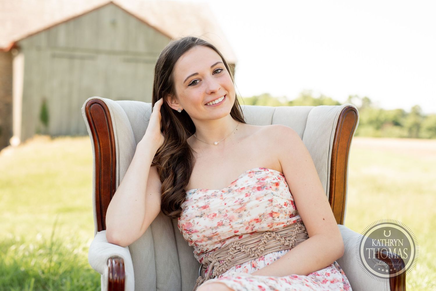Elegant summer portrait in cream armchair with rustic barn backdrop.