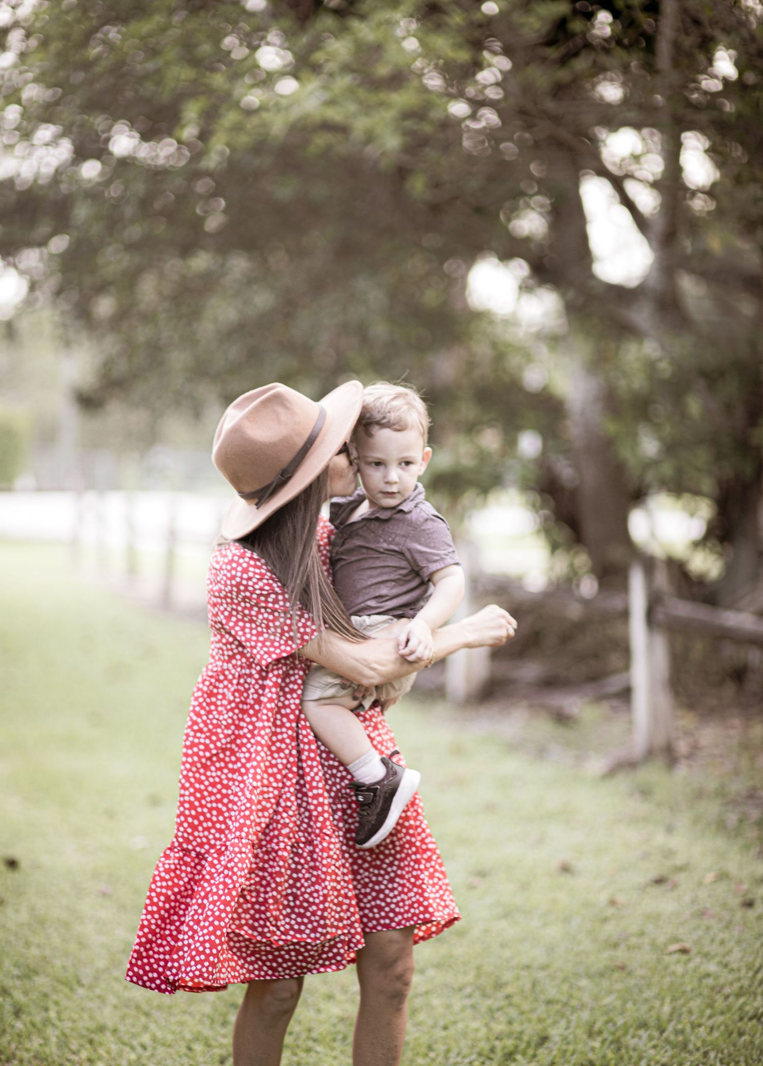 Woman in red polka dot dress holding child in outdoor garden setting.