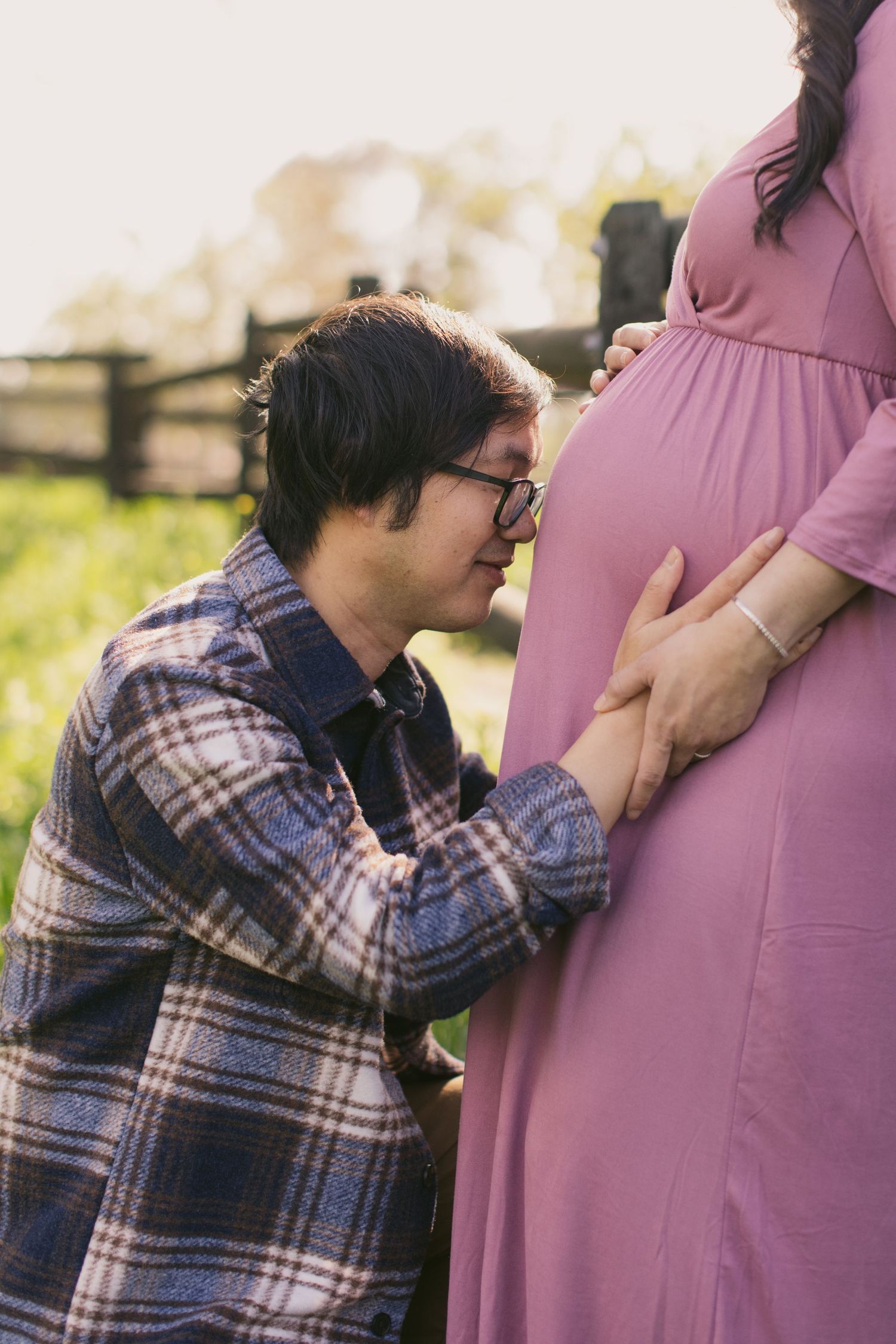 Intimate maternity moment captured with couple in casual attire by wooden fence.