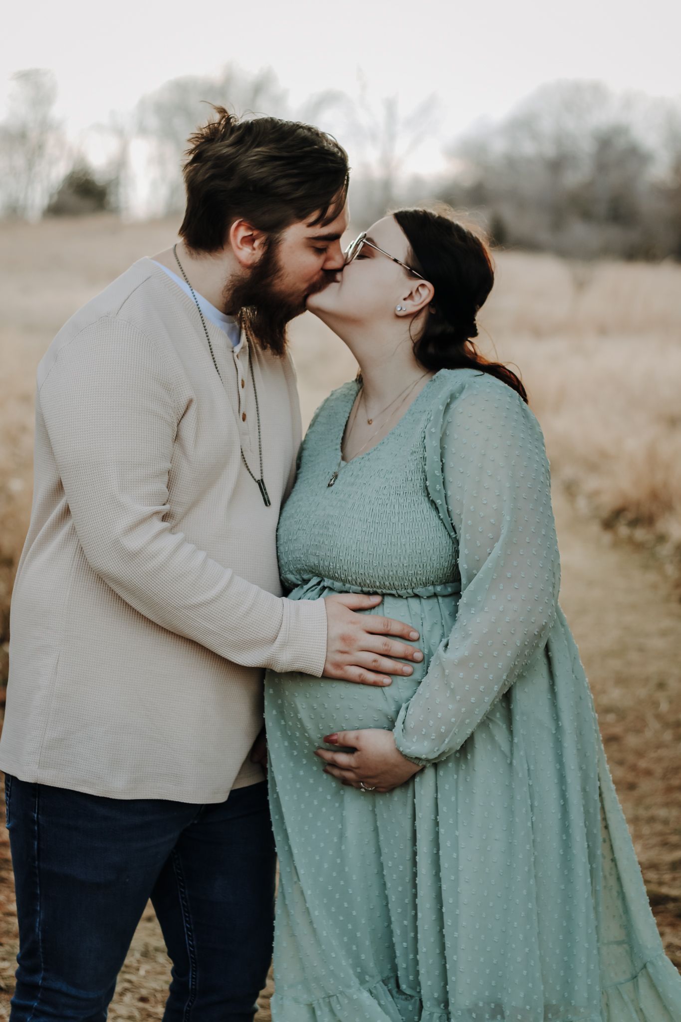 A couple sharing an intimate moment outdoors with a pregnant woman in a mint green dress.