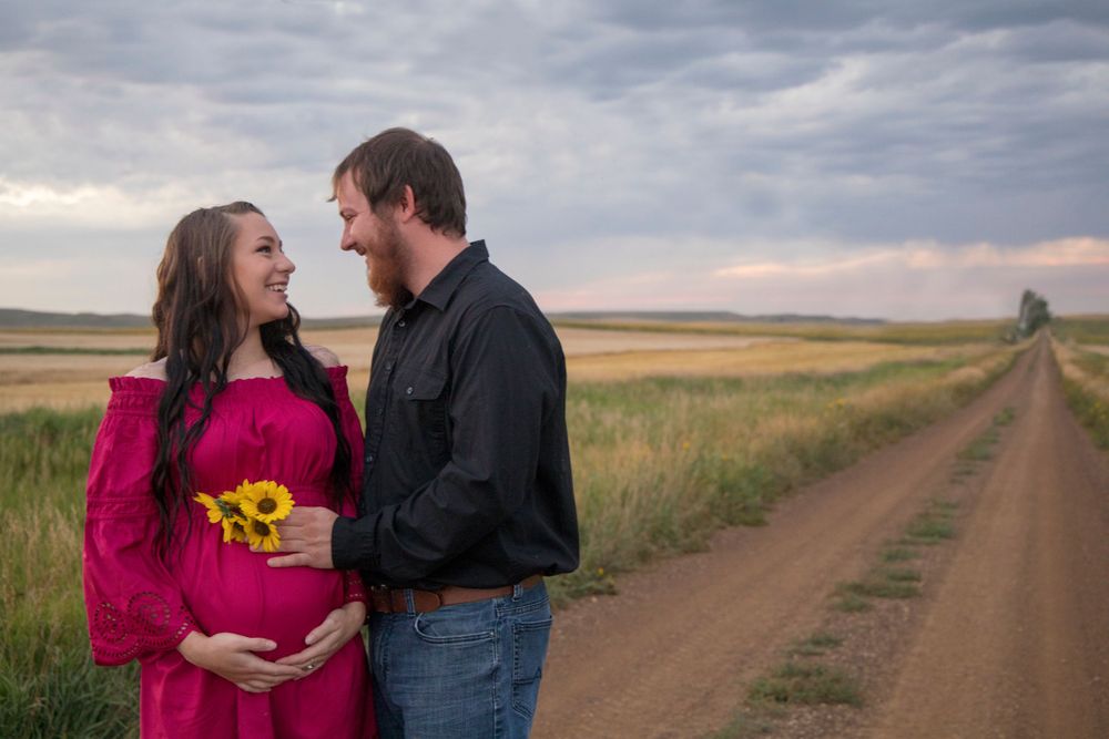 Couple sharing a moment with sunflowers on a rural dirt road at dusk.