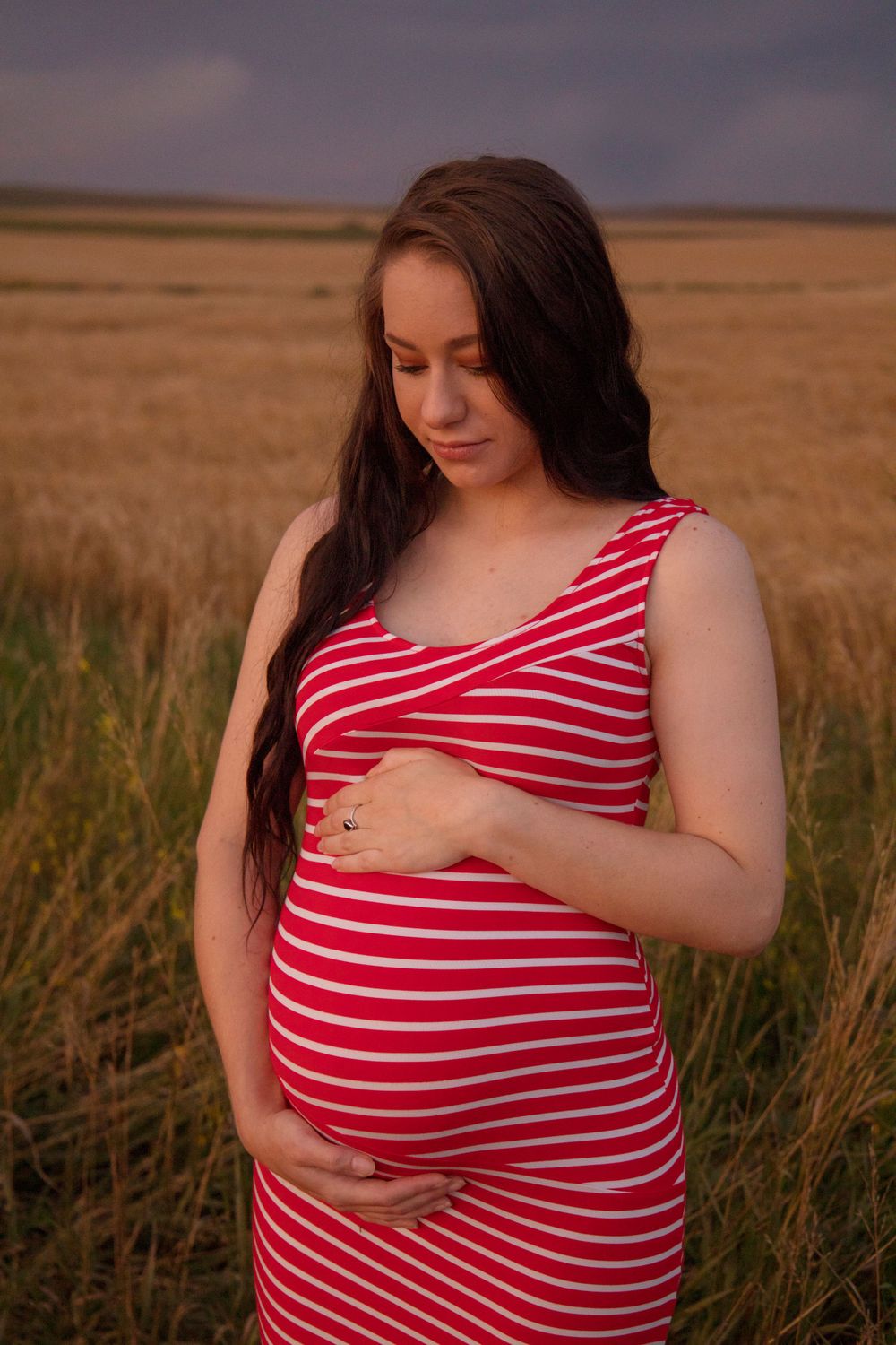 Someone in a red striped dress stands thoughtfully in a field at dusk.