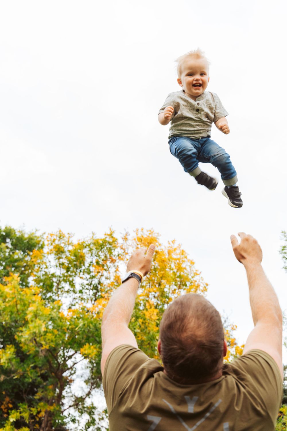 Baby being tossed in the air while laughing with fall trees in the background.