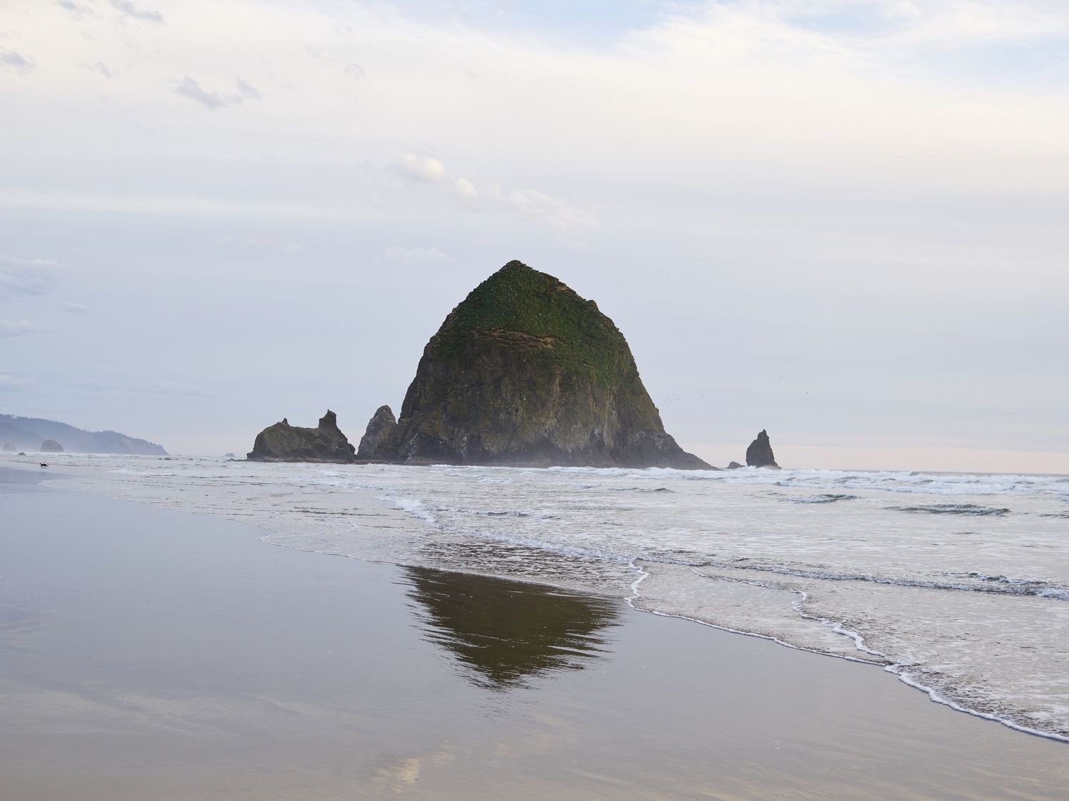 Cloudy day at Cannon Beach, Oregon. Calm ocean reflects Haystack rock.
