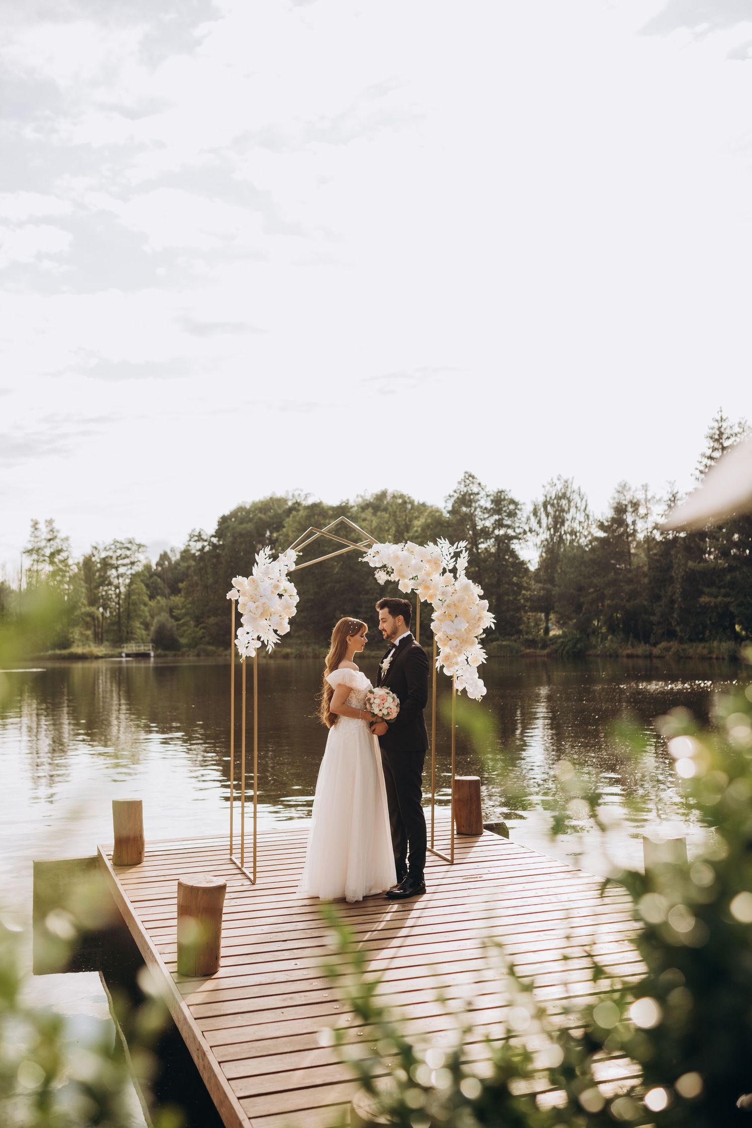 Wedding ceremony setup on a wooden dock over a lake with floral arch decorations.