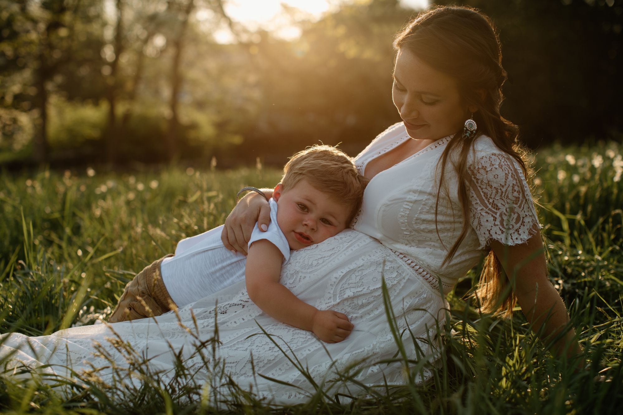 Intimate maternity photos taken in golden sunlit field with soft natural lighting.