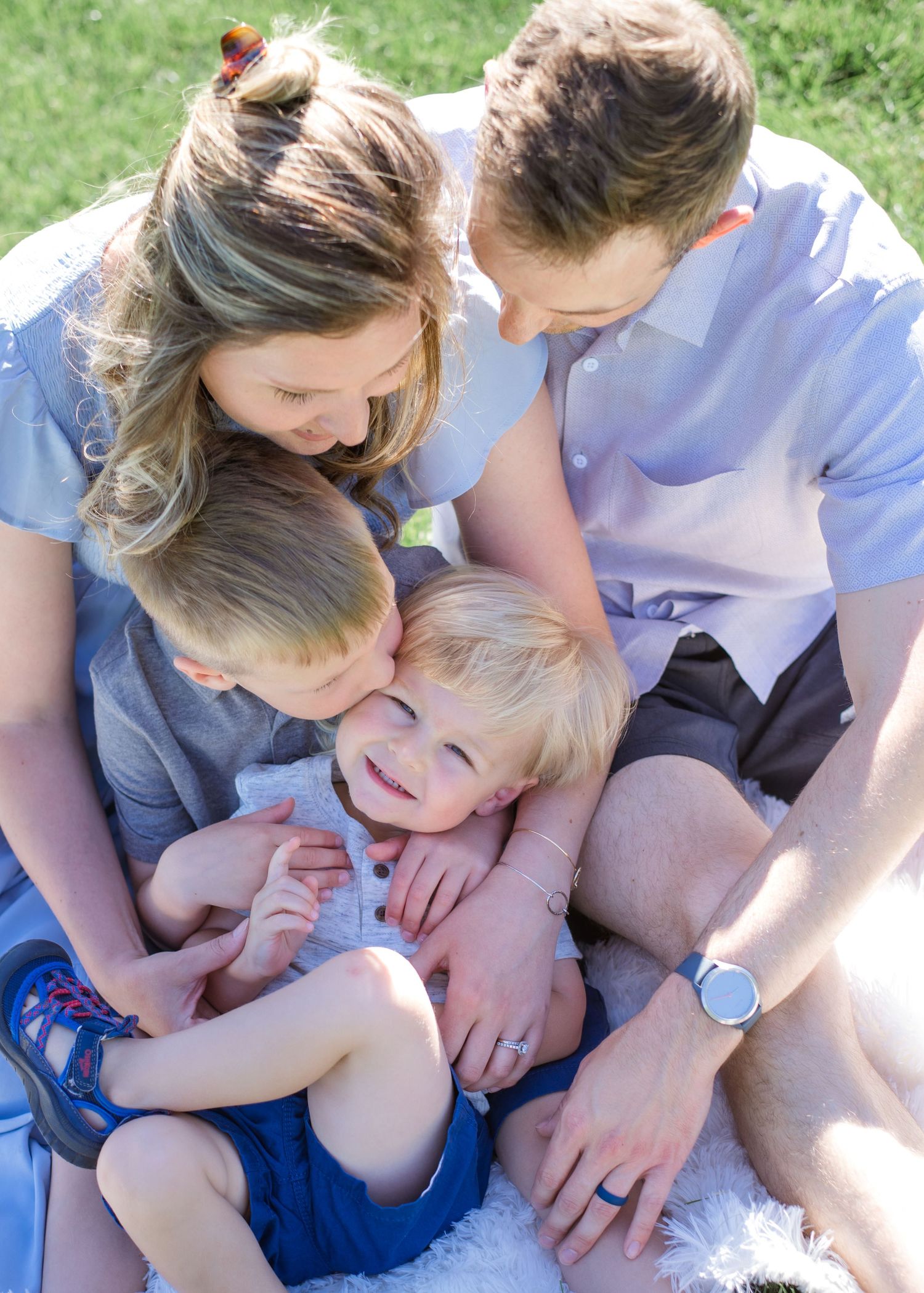 A family shares cuddles and laughter while sitting together on grass in the sunshine.
