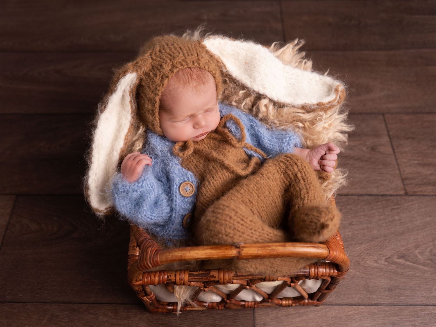 Newborn baby boy wearing peter rabbit outfit, in a rattan basket with fluffy blankets at newborn photoshoot in Doncaster