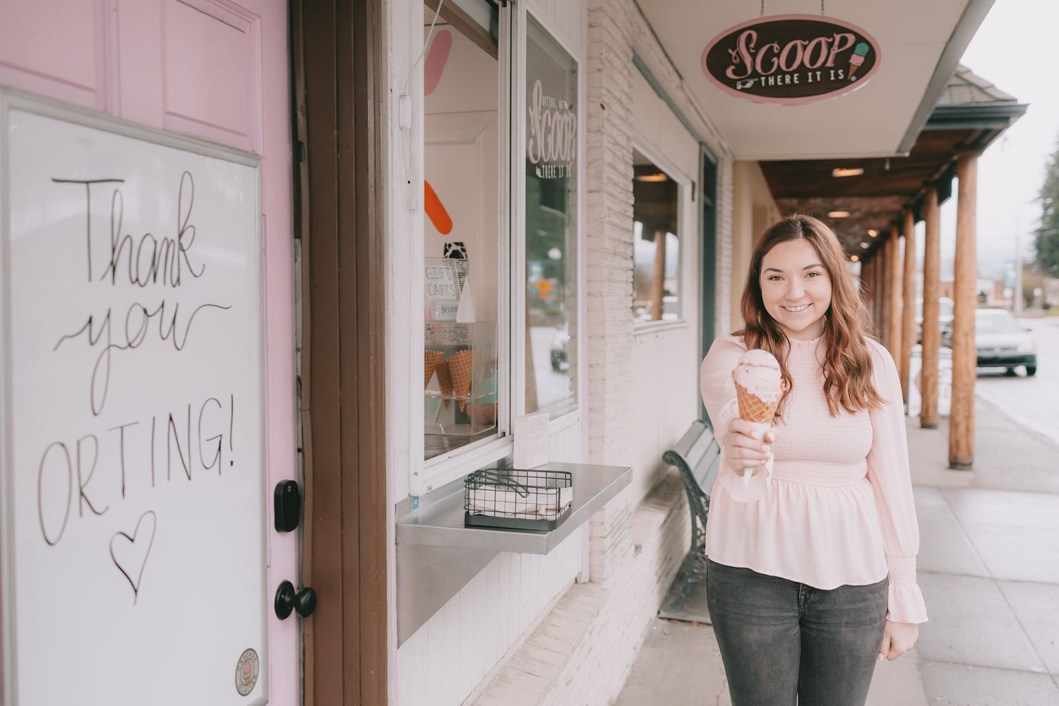 A white board that says Thank You Orting Heart a woman under a sign that says Scoop she is holding an ice cream cone.