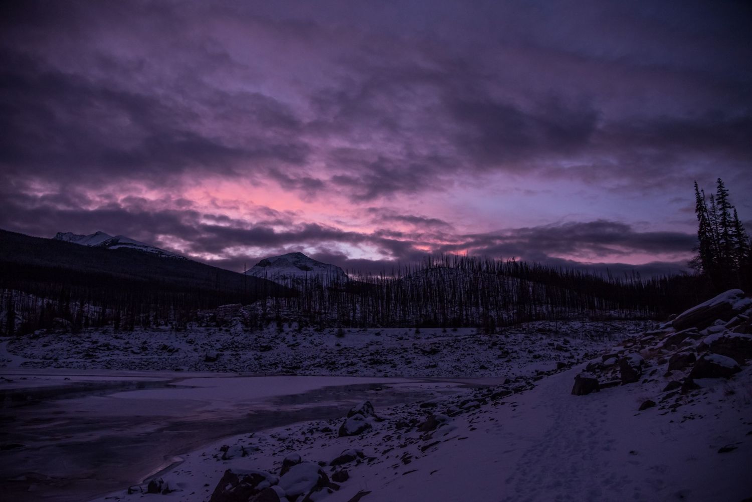 Purple and pink sunset sky over snowy mountain landscape.