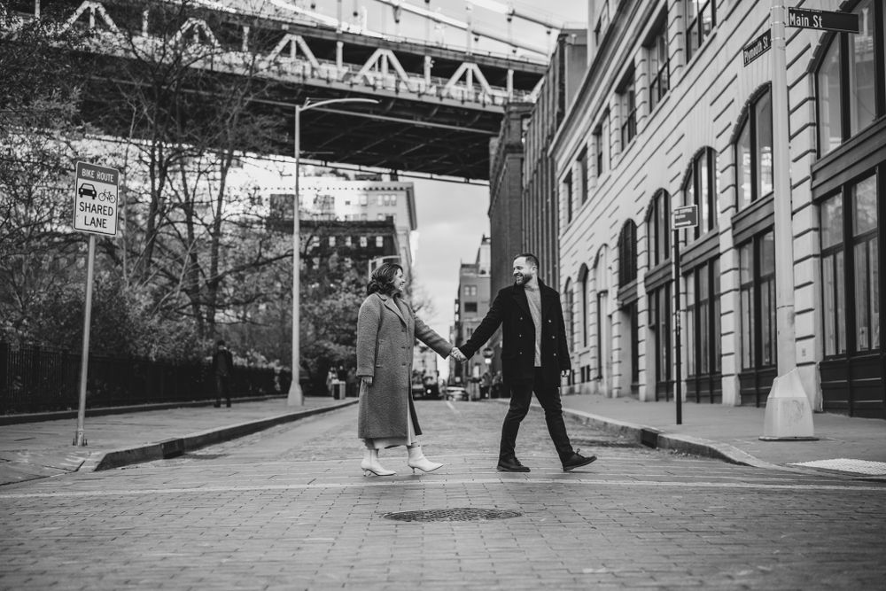 A couple walks along an urban street with buildings and trees.